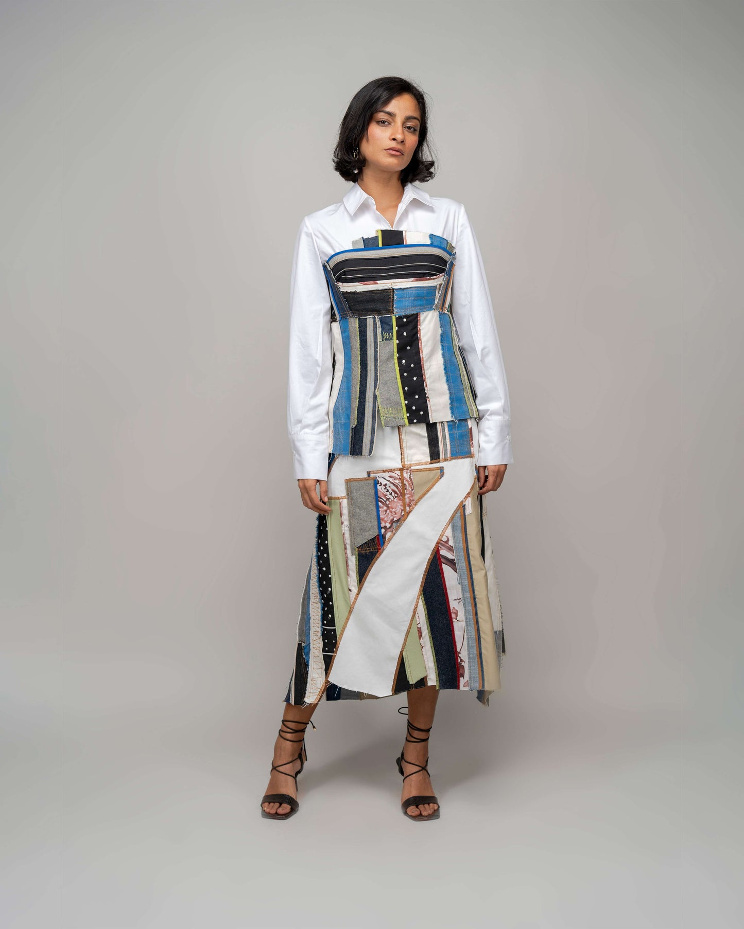 A model wearing a multicolored patchwork skirt with an asymmetrical hemline and side pockets, paired with a white top.