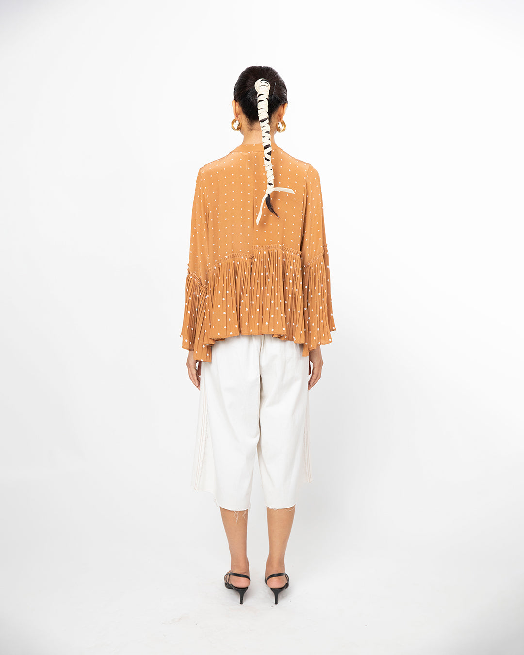 Person wearing a mustard yellow fringed top and white pants on a white background from Leh Studios.