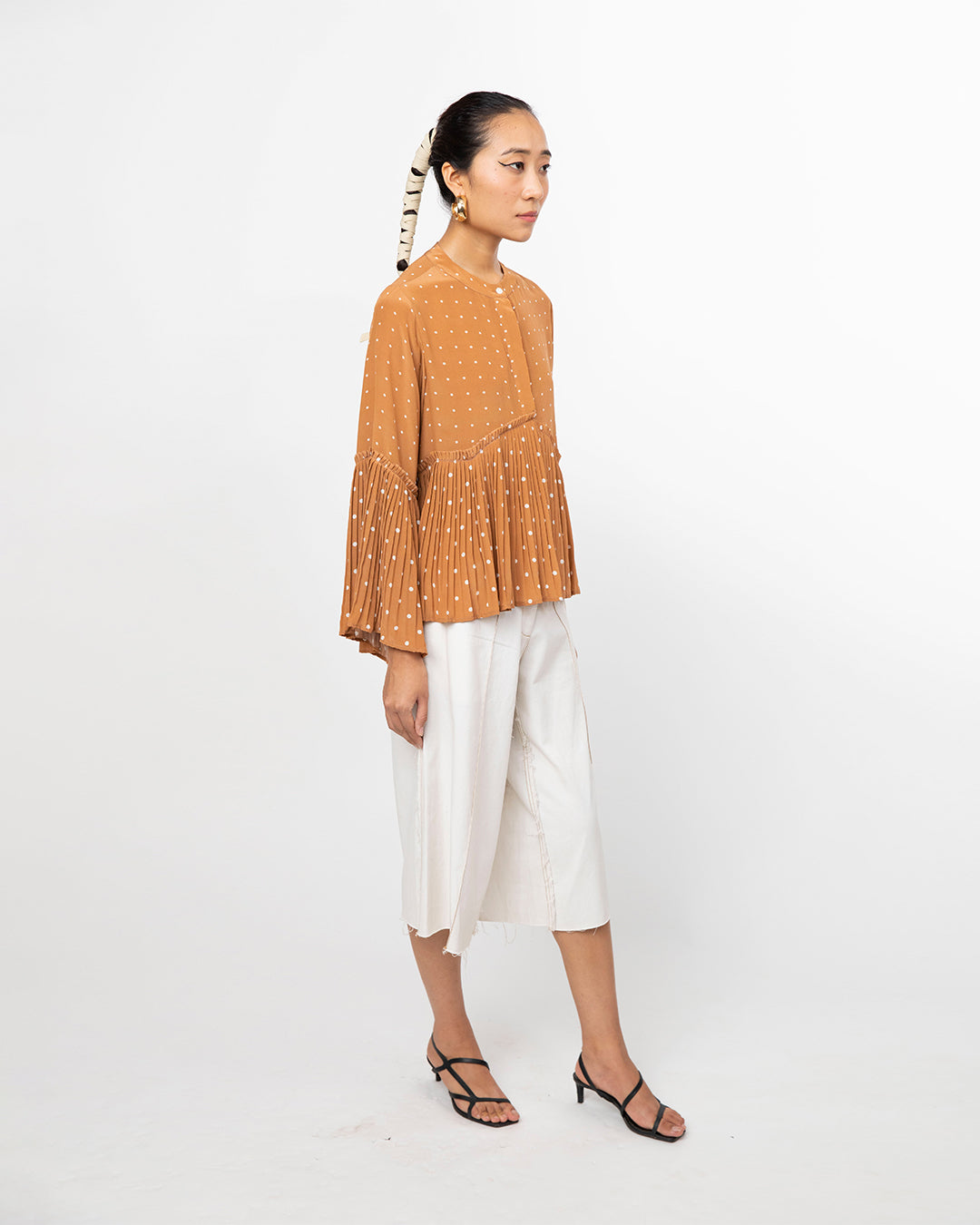 Woman wearing a mustard yellow top with bead details and white pants on a white background from Leh Studios.