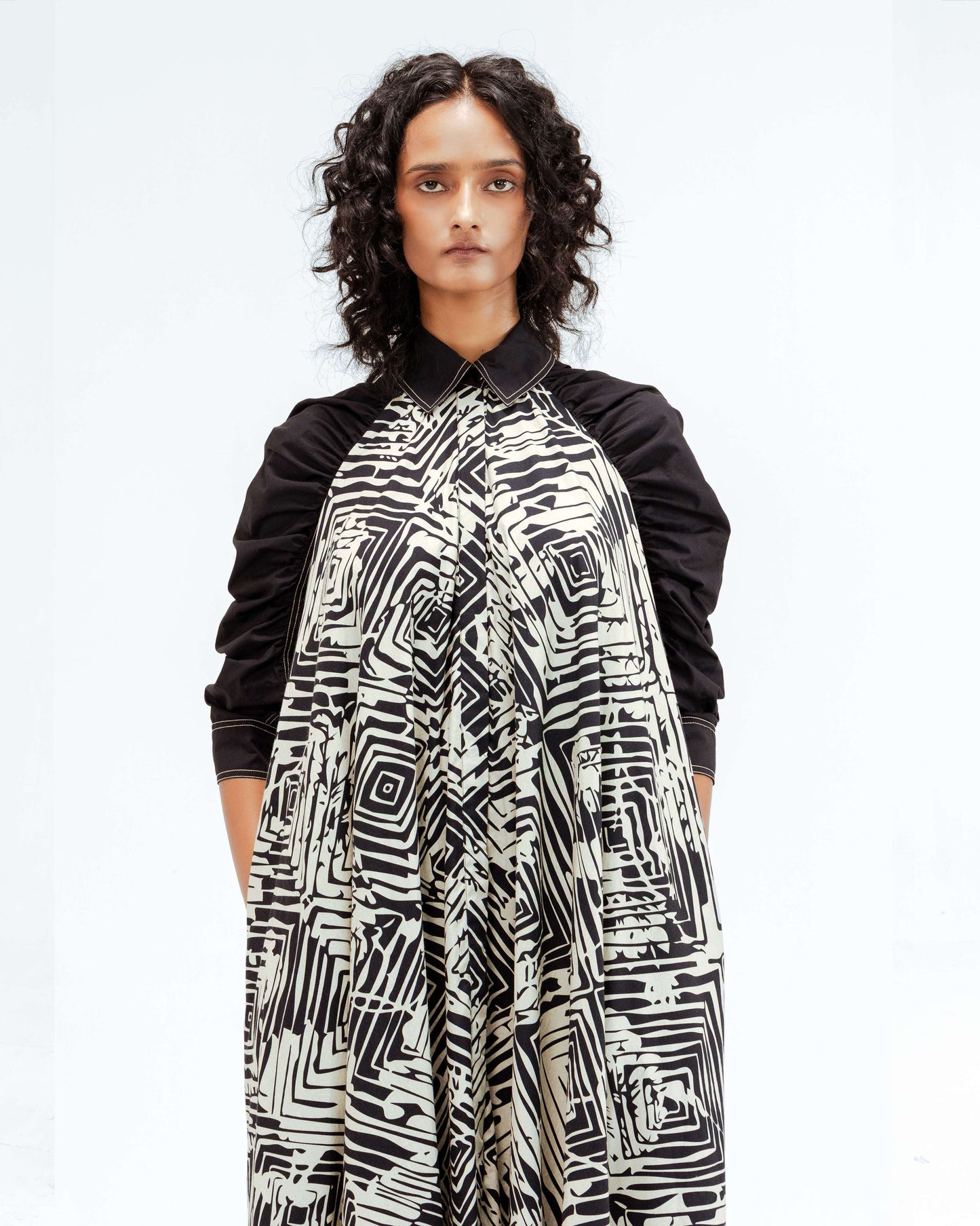 A model showcases the Leh Studios Florix Print Fable Dress from the Rhythm of time collection, featuring a striking black and white abstract geometric pattern on a loose, flowy silhouette with black puffy sleeves and collar. This designer wear exemplifies sustainable fashion and eco-friendly design, crafted from organic cotton for a chic womens apparel statement.