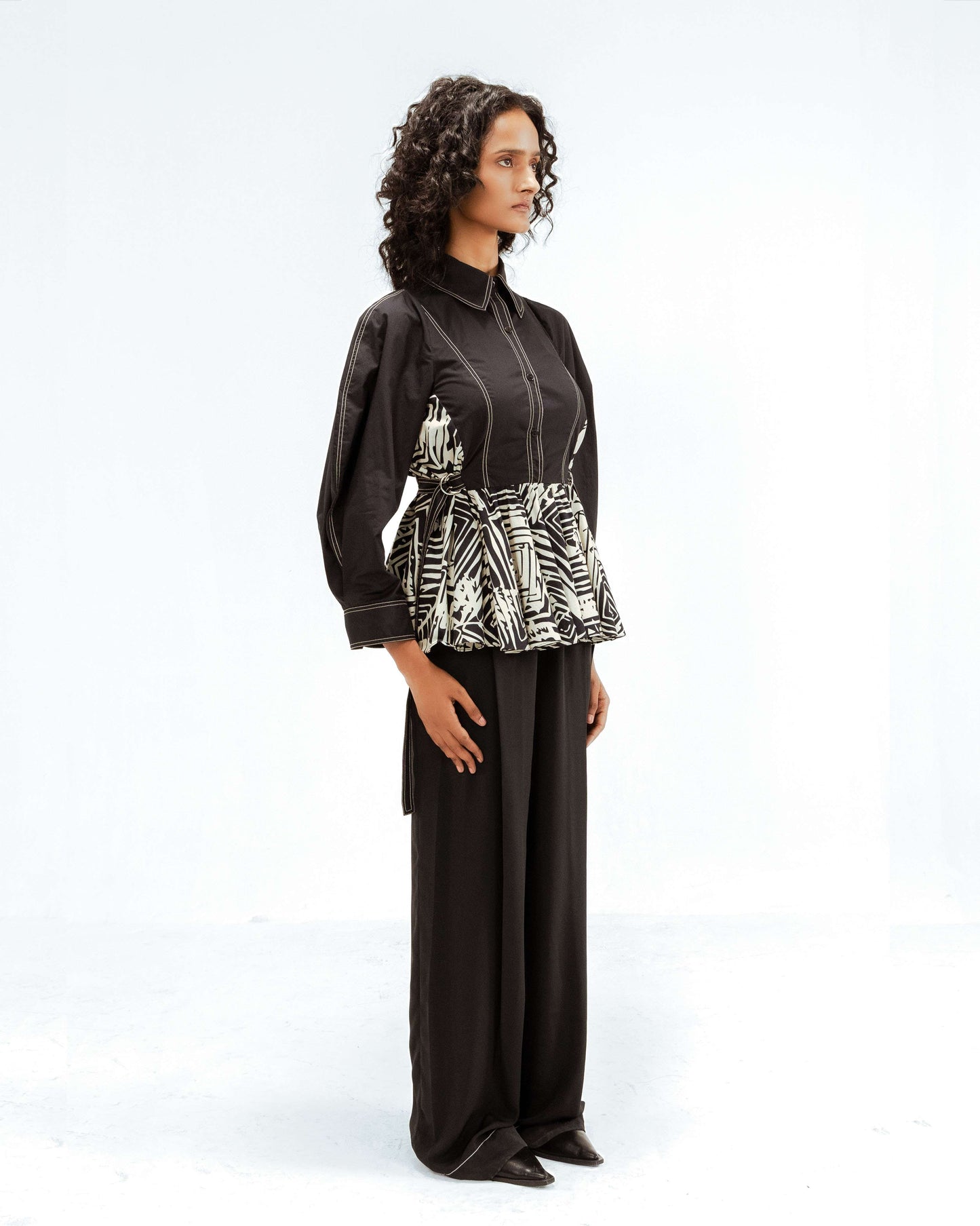 Model showcasing the Leh Studios Fable top from the Rhythm of time collection, a black button-up with elegant white contrast stitching and a peplum hem featuring an abstract black and white pattern, reflecting sustainable fashion and artisanal craftsmanship in luxury womens apparel.