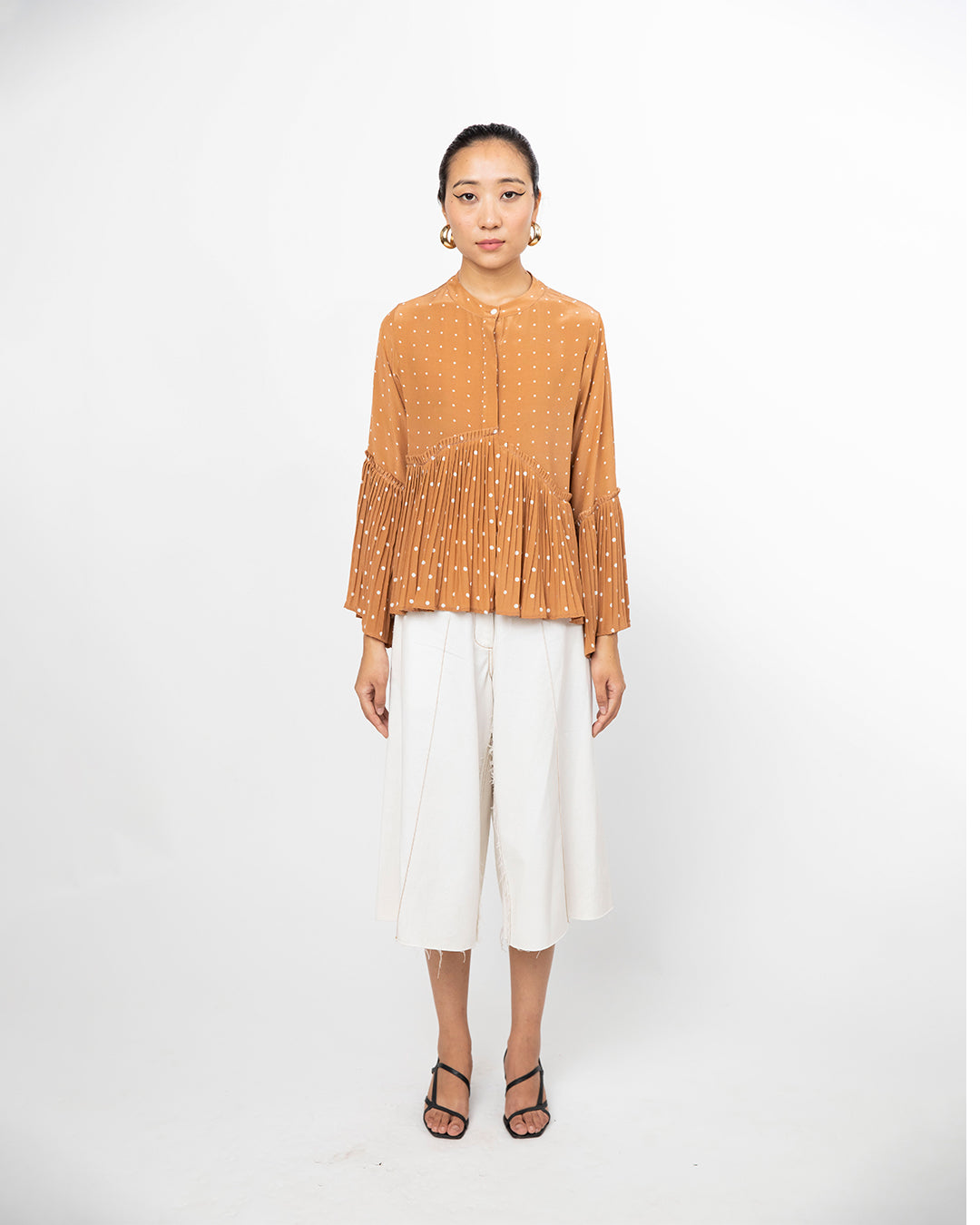 Woman wearing a mustard yellow blouse and white pants on a white background from Leh Studios.