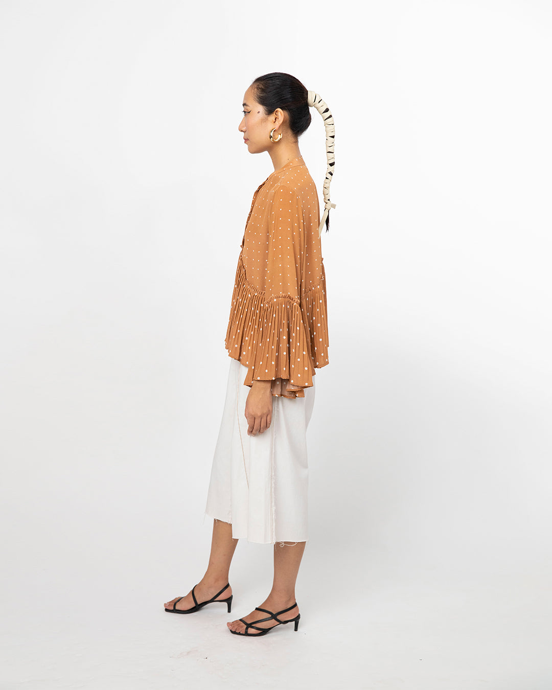 Woman wearing a mustard yellow top and white pants on a white background from Leh Studios.