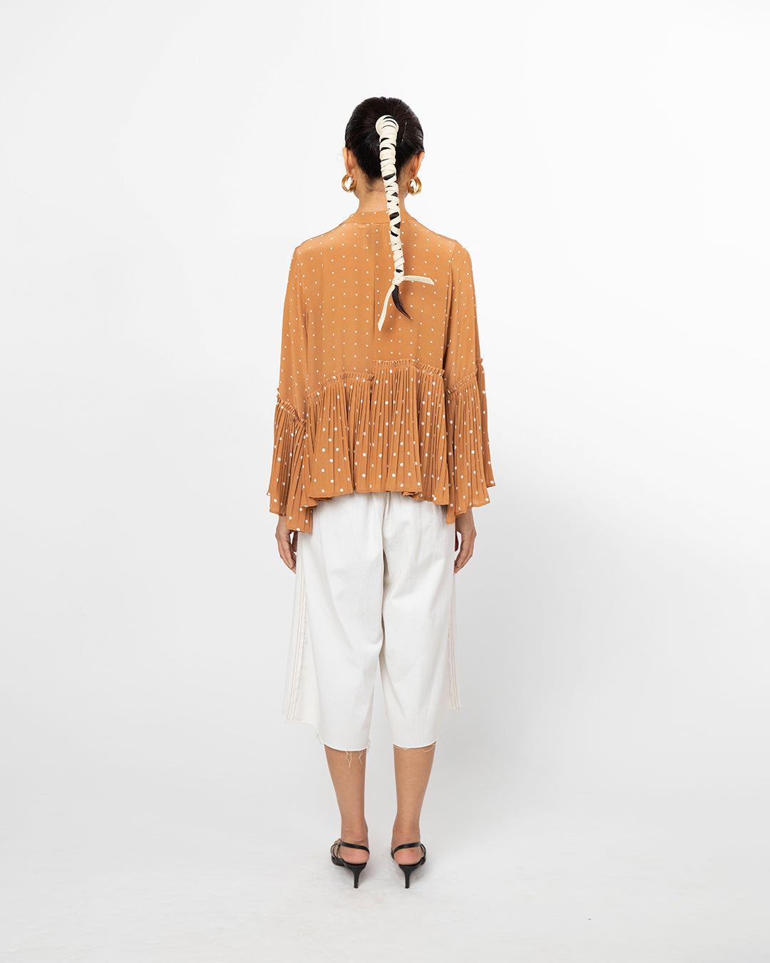 Person wearing a mustard yellow textured top and white pants on a white background from Leh Studios.
