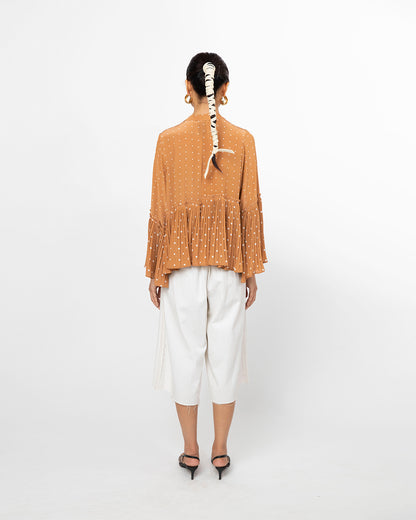 Person wearing a mustard yellow textured top and white pants on a white background from Leh Studios.