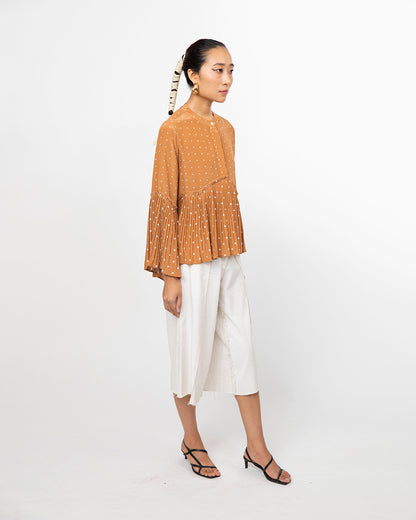 Woman wearing a mustard yellow top with bead details and white pants on a white background from Leh Studios.