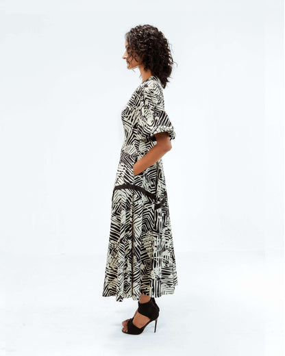 Leh Studios Florix Print Thalia Dress from the Rhythm of time collection, featuring an elegant black and off-white abstract pattern. This sustainable fashion piece offers contemporary designer wear for women, made with an eco-friendly design. The model stands in profile, showcasing the dress's sophisticated silhouette, puffed sleeves, and practical pockets.