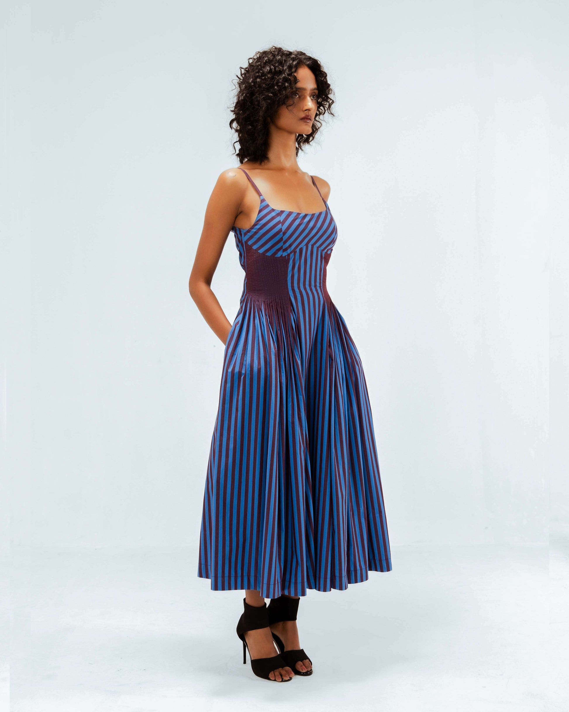 The Leh Studios Meva Dress, part of the Rhythm of time collection, features a striking blue and maroon striped pattern with a distinct pleated waist detail. This upcycled clothing piece represents eco-friendly design, blending contemporary style with sustainable Indian fashion for the modern woman.