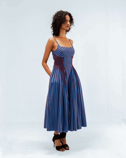The Leh Studios Meva Dress, part of the Rhythm of time collection, features a striking blue and maroon striped pattern with a distinct pleated waist detail. This upcycled clothing piece represents eco-friendly design, blending contemporary style with sustainable Indian fashion for the modern woman.