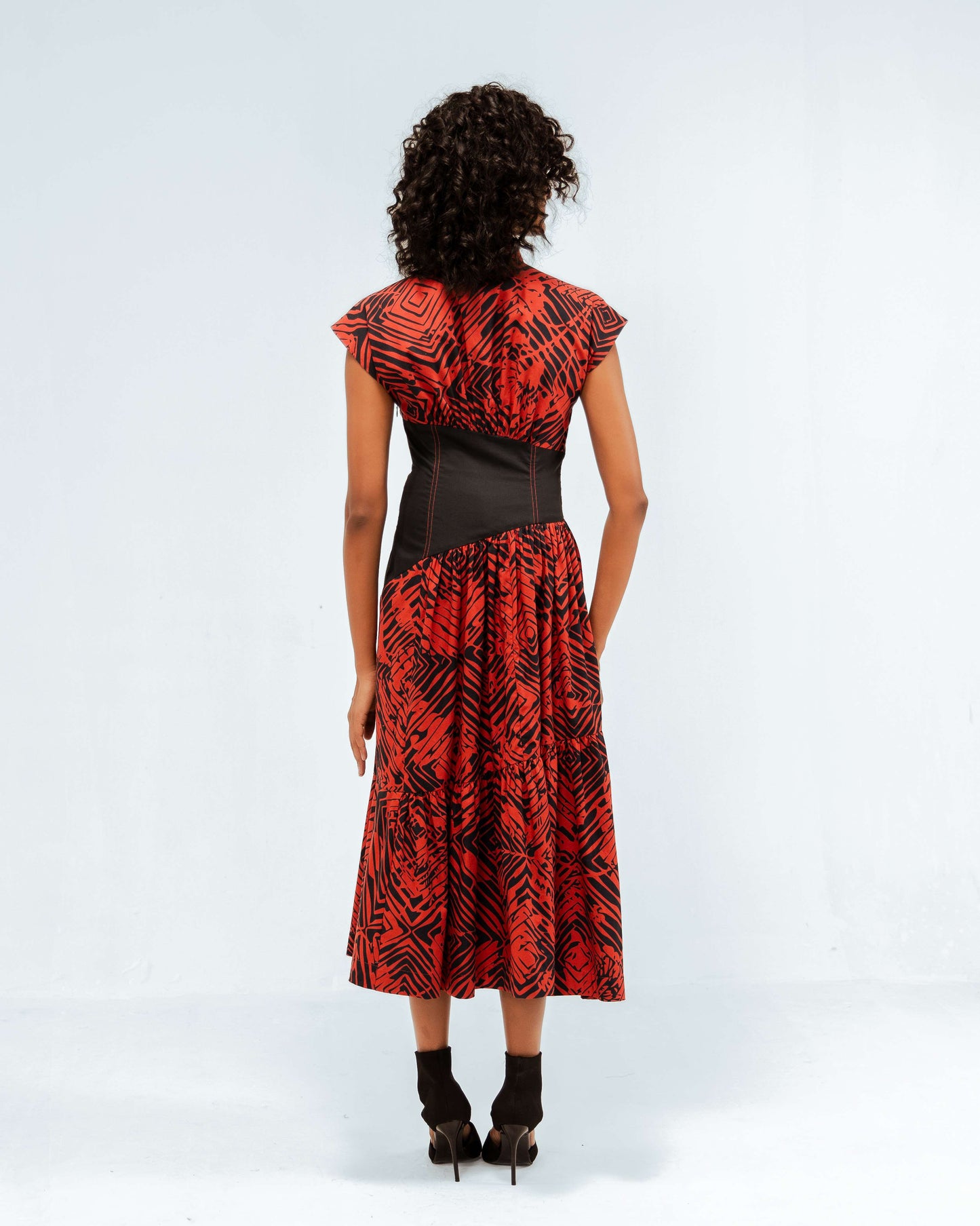 The Leh Studios Florix Print Basque Tiered Dress in red and black abstract print, viewed from the back on a model. This midi dress from the Rhythm of time collection highlights artisanal craftsmanship and eco-friendly design, representing luxury upcycled clothing that blends Indian traditions with contemporary leh clothing.