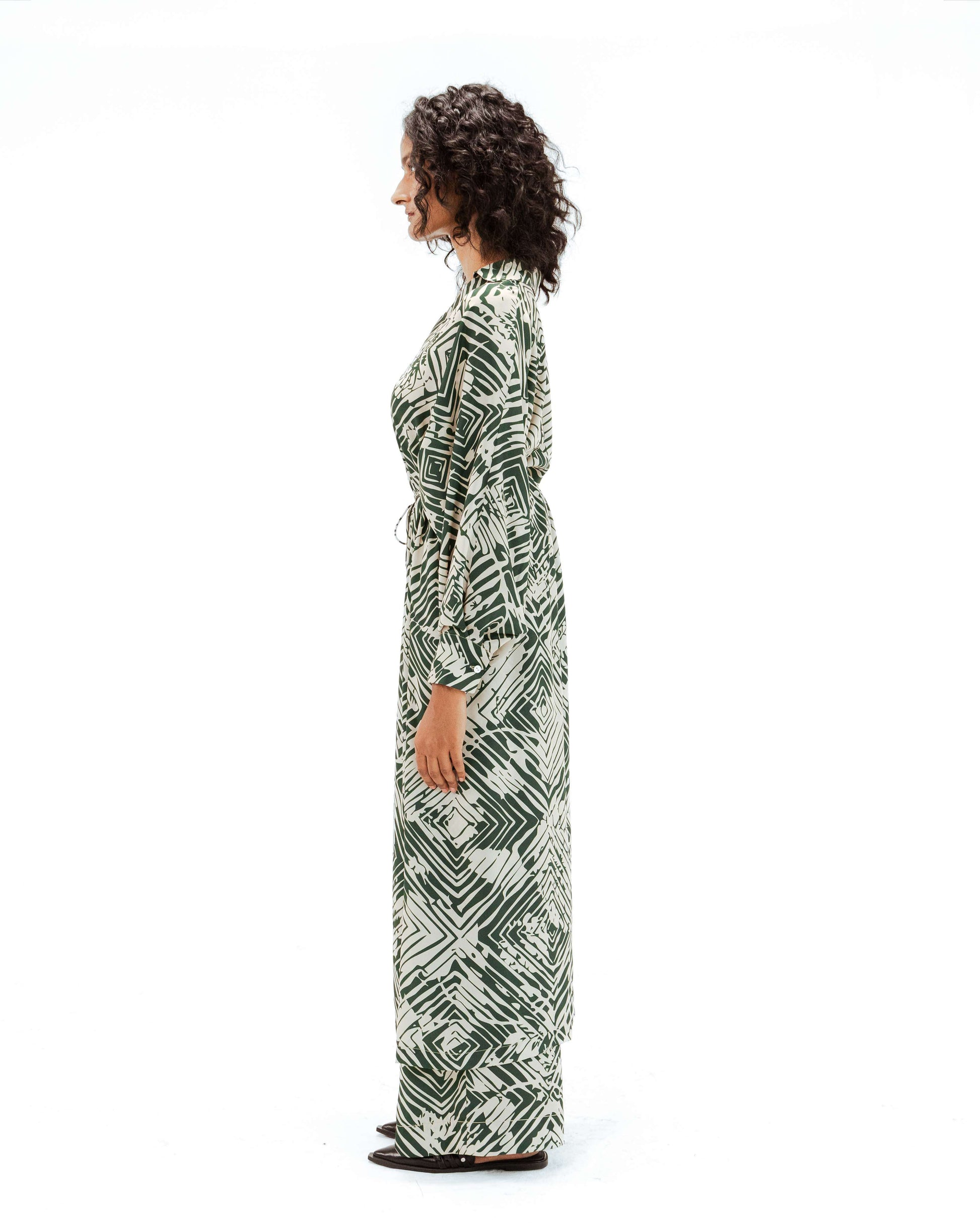 The Leh Studios Florix Print Crepe Cape Dress, an exquisite piece of handcrafted apparel from the Rhythm of time collection, showcased on a model. Its unique green geometric pattern on off-white fabric reflects artisanal craftsmanship, embodying ethical fashion and sustainable Indian fashion principles.