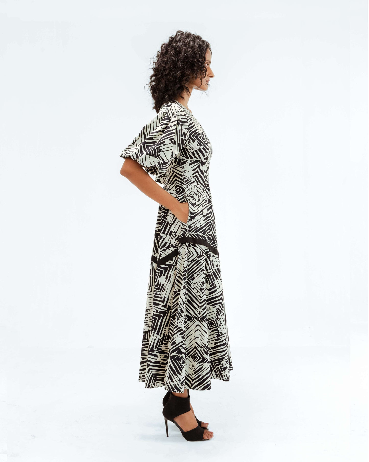 Profile view of a model wearing the Leh Studios Florix Print Thalia Dress, a striking black and off-white patterned midi dress from the Rhythm of time collection. This luxury upcycled fashion item represents ethical fashion and handcrafted apparel, showcasing exquisite artisanal craftsmanship.