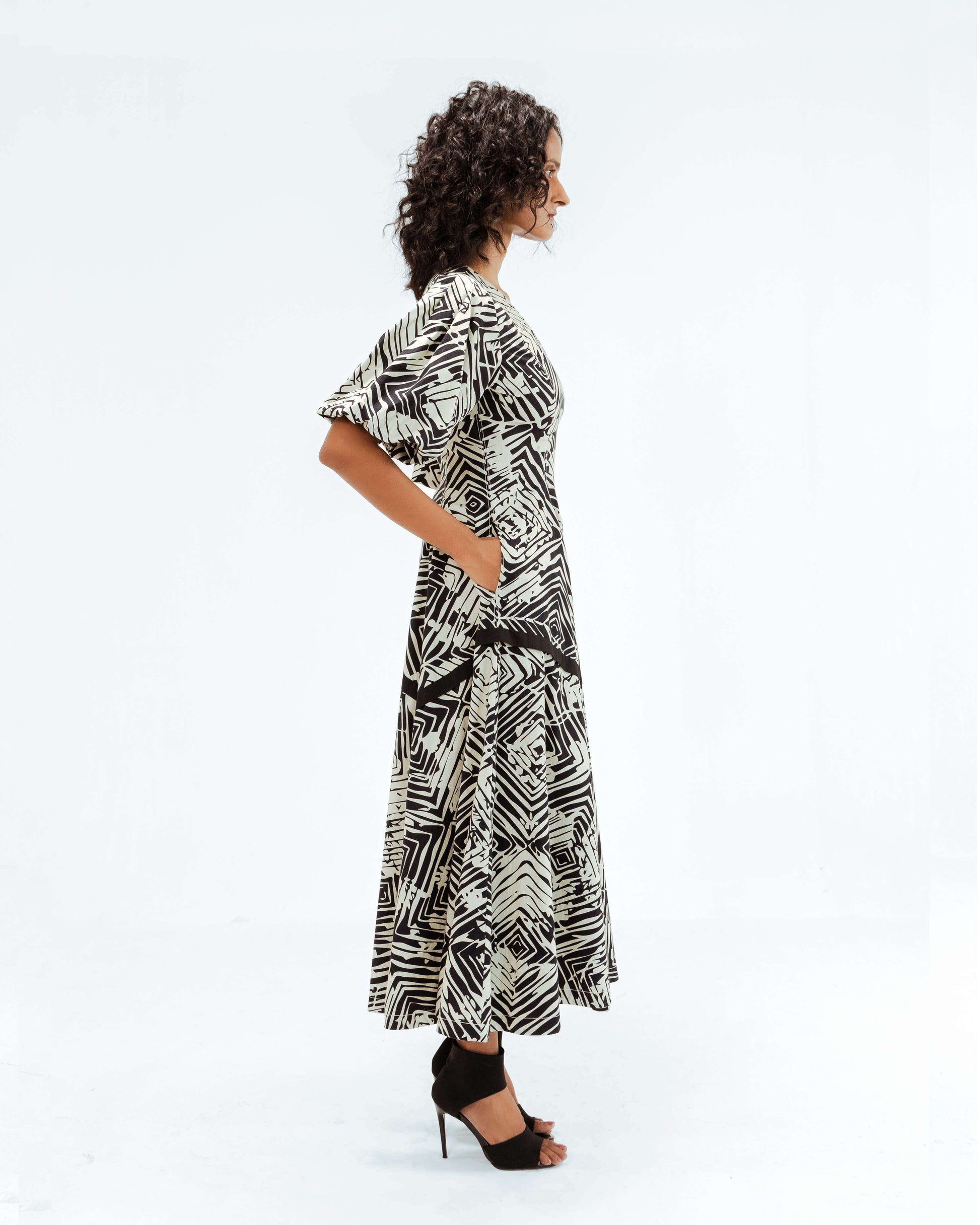 Profile view of a model wearing the Leh Studios Florix Print Thalia Dress, a striking black and off-white patterned midi dress from the Rhythm of time collection. This luxury upcycled fashion item represents ethical fashion and handcrafted apparel, showcasing exquisite artisanal craftsmanship.