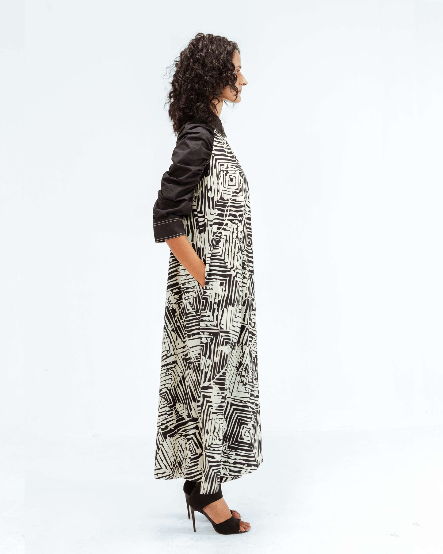 Experience the luxury upcycled fashion of Leh Studios with the Florix Print Fable Dress from the Rhythm of time collection. This elegant Leh clothing piece, worn by a model, features a captivating black and white geometric pattern, structured black collar and puffy sleeves, showcasing handcrafted apparel that embodies responsible creativity and sophisticated womenswear.