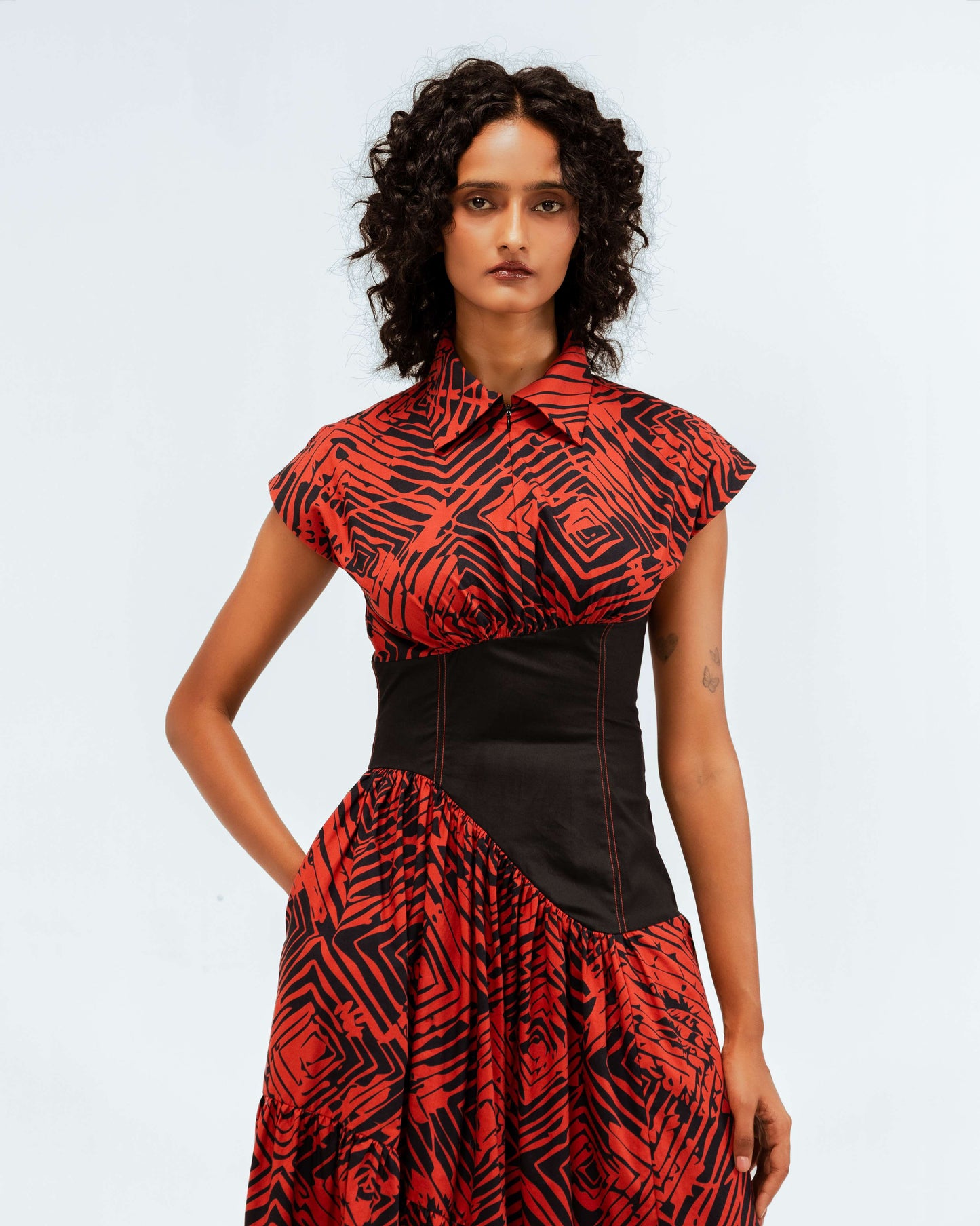 Model wears the Leh Studios Florix Print Basque Tiered Dress from the Rhythm of time collection. This designer wear features a vibrant red and black abstract print, a collared top, short sleeves, a structured black basque waist, and a tiered skirt, embodying sustainable fashion with potential organic cotton for womens apparel.