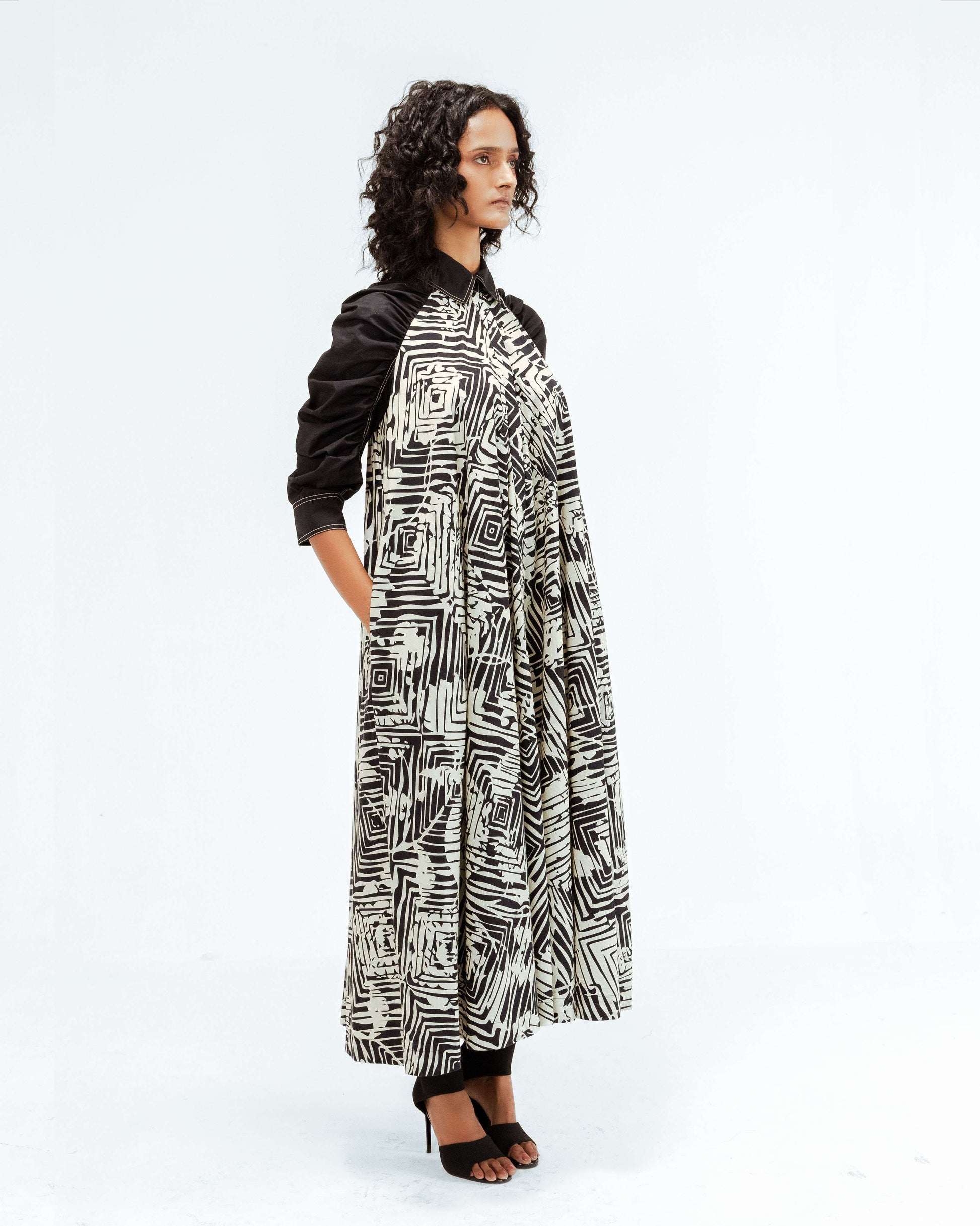 The Leh Studios Florix Print Fable Dress, part of the Rhythm of time collection, displayed on a model, highlights a unique black and white abstract print on a comfortable, billowy design with contrasting black sleeves. This upcycled clothing piece reflects artisanal craftsmanship and ethical fashion, offering sophisticated womens apparel that blends Indian traditions with contemporary style.