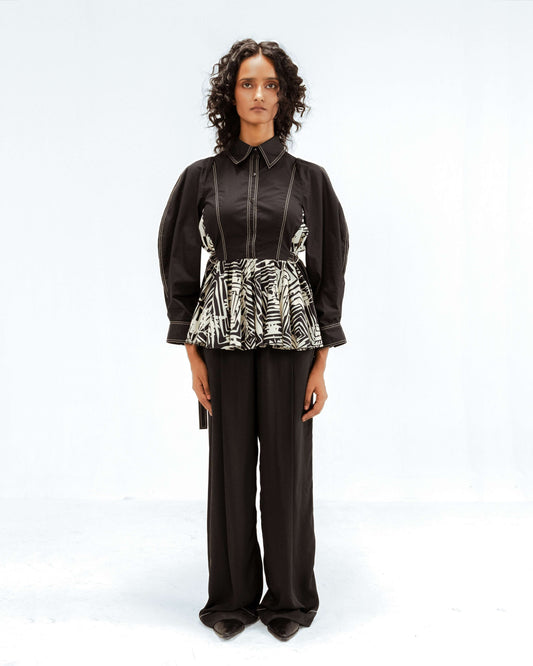 A model wears the Leh Studios Fable top from the Rhythm of Time collection, featuring a black collared bodice with contrast stitching and voluminous sleeves, combined with a peplum-style hem in a black and off-white abstract print. This upcycled clothing exemplifies sustainable fashion and represents luxury designer wear for women.