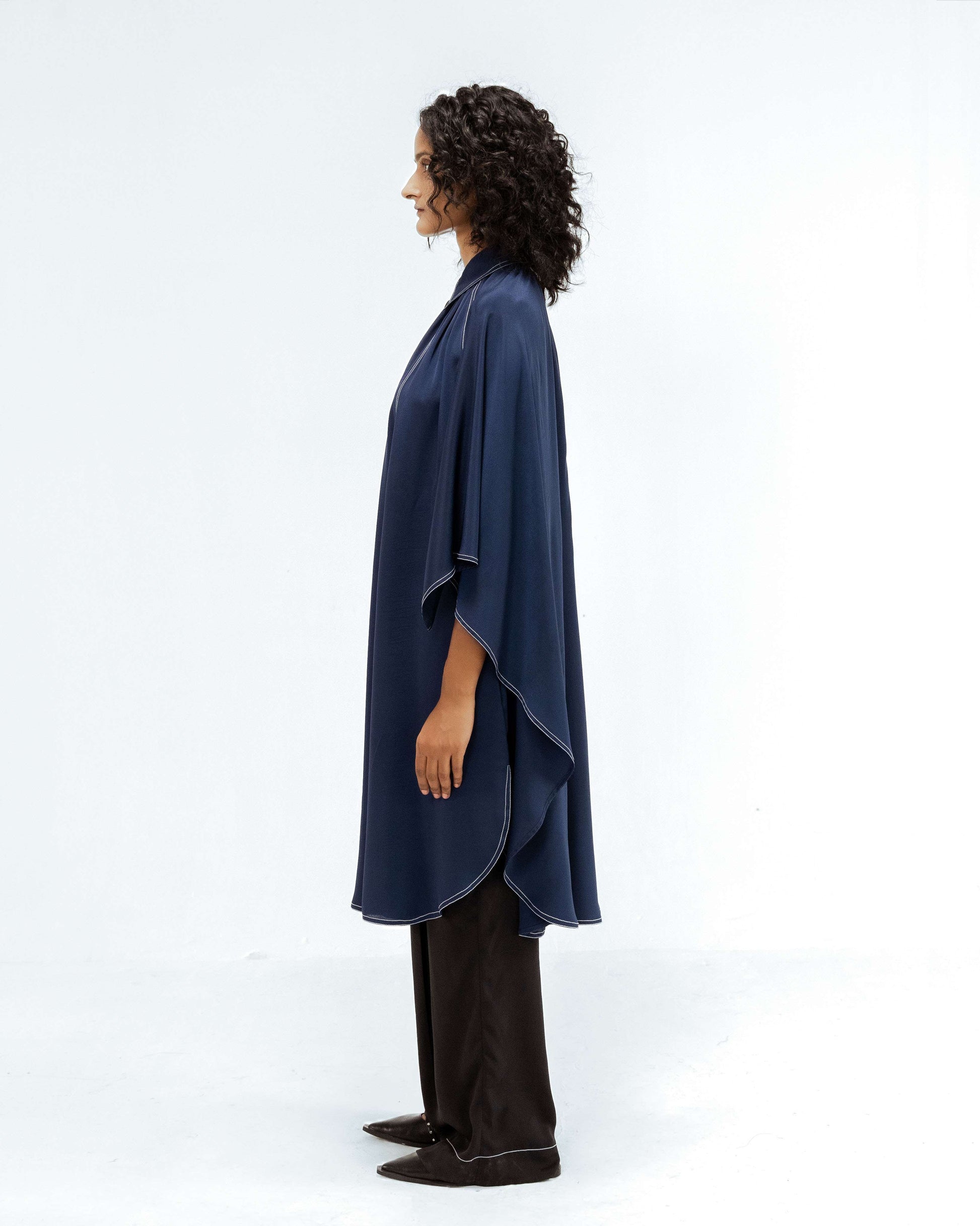 A model in profile showcases the Leh Studios Selene Crepe Set from the Rhythm of time collection, featuring a dark blue sustainable tunic top with white contrast stitching and matching black trousers. This elegant womens apparel highlights eco-friendly design and contemporary Indian fashion.