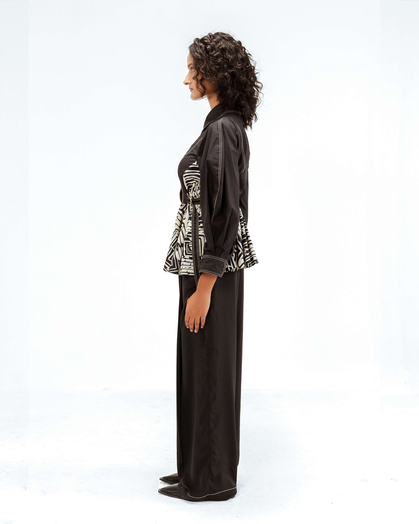 The Leh Studios Fable top, styled here on a model in profile, is a black designer wear item with an eye-catching upcycled geometric patterned waist and delicate white topstitching, offering luxury upcycled fashion and eco-friendly design.