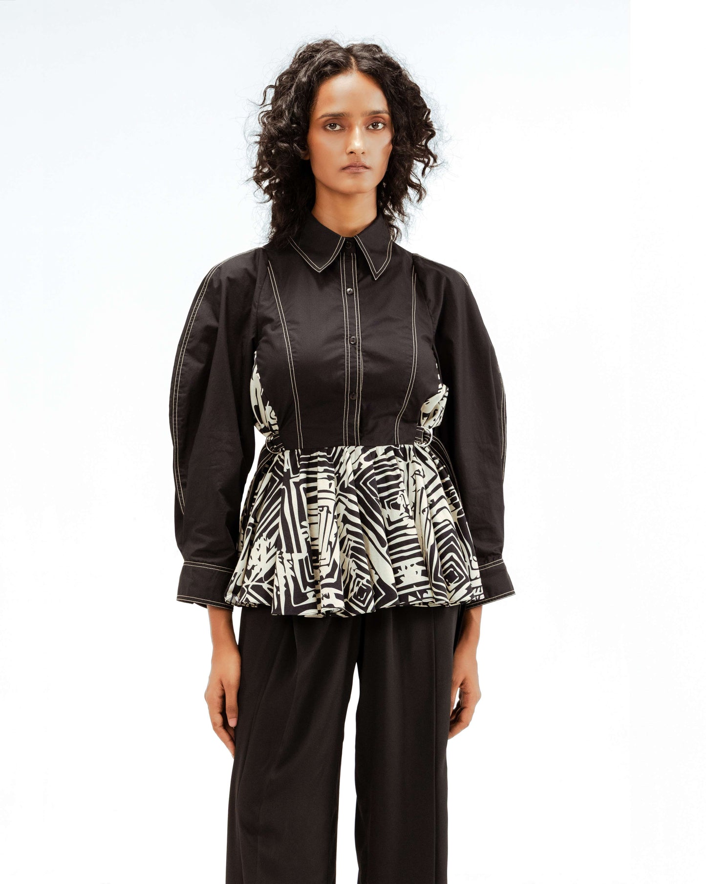 Leh Studios presents the Fable top, a unique piece of sustainable Indian fashion from the Rhythm of Time collection. This collared black top boasts puffed sleeves and a gathered peplum with an intricate black and white pattern, highlighting eco-friendly design and luxury upcycled fashion.