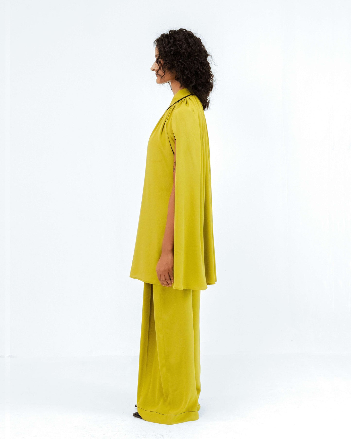 A model stands in profile, showcasing the Leh Studios Cherice Crepe Cordset in a vibrant chartreuse green. This sustainable fashion designer wear from the Rhythm of time collection features a flowing, cape-style top and wide-leg pants, embodying eco-friendly design and modern womens apparel.