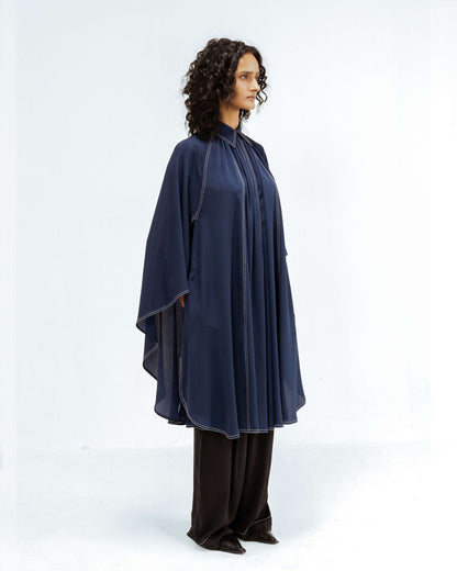 A model showcases the Leh Studios Selene Crepe Set from the Rhythm of time collection. This elegant navy blue sustainable fashion top features a high collar and flowing silhouette with distinctive white contrast stitching, paired with complementary black trousers. The outfit exemplifies artisanal craftsmanship and contemporary designer wear.