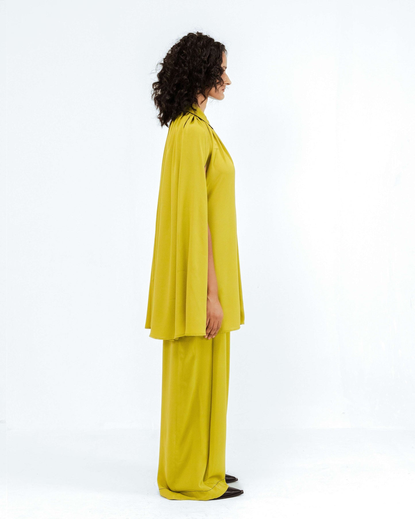 A model in profile showcases the lime green Cherice Crepe Cordset from Leh Studios Rhythm of time collection, featuring a luxurious cape-style top and wide-leg pants. This elegant ensemble highlights Leh Studios commitment to sustainable fashion and eco-friendly design in womens apparel.