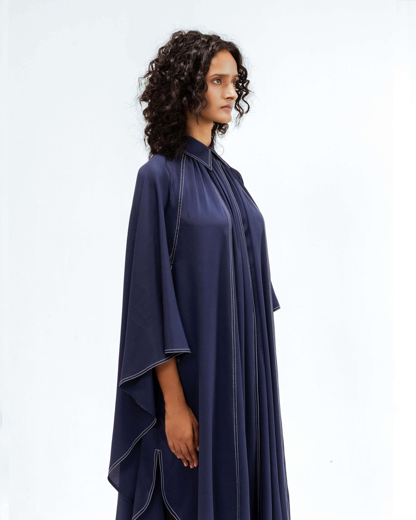 A model in profile showcases the Leh Studios Selene Crepe Set, a flowing navy blue top with distinctive white contrast stitching, embodying contemporary design and artisanal craftsmanship from the Rhythm of time collection. This luxury upcycled fashion piece offers sustainable Indian fashion for womens apparel.