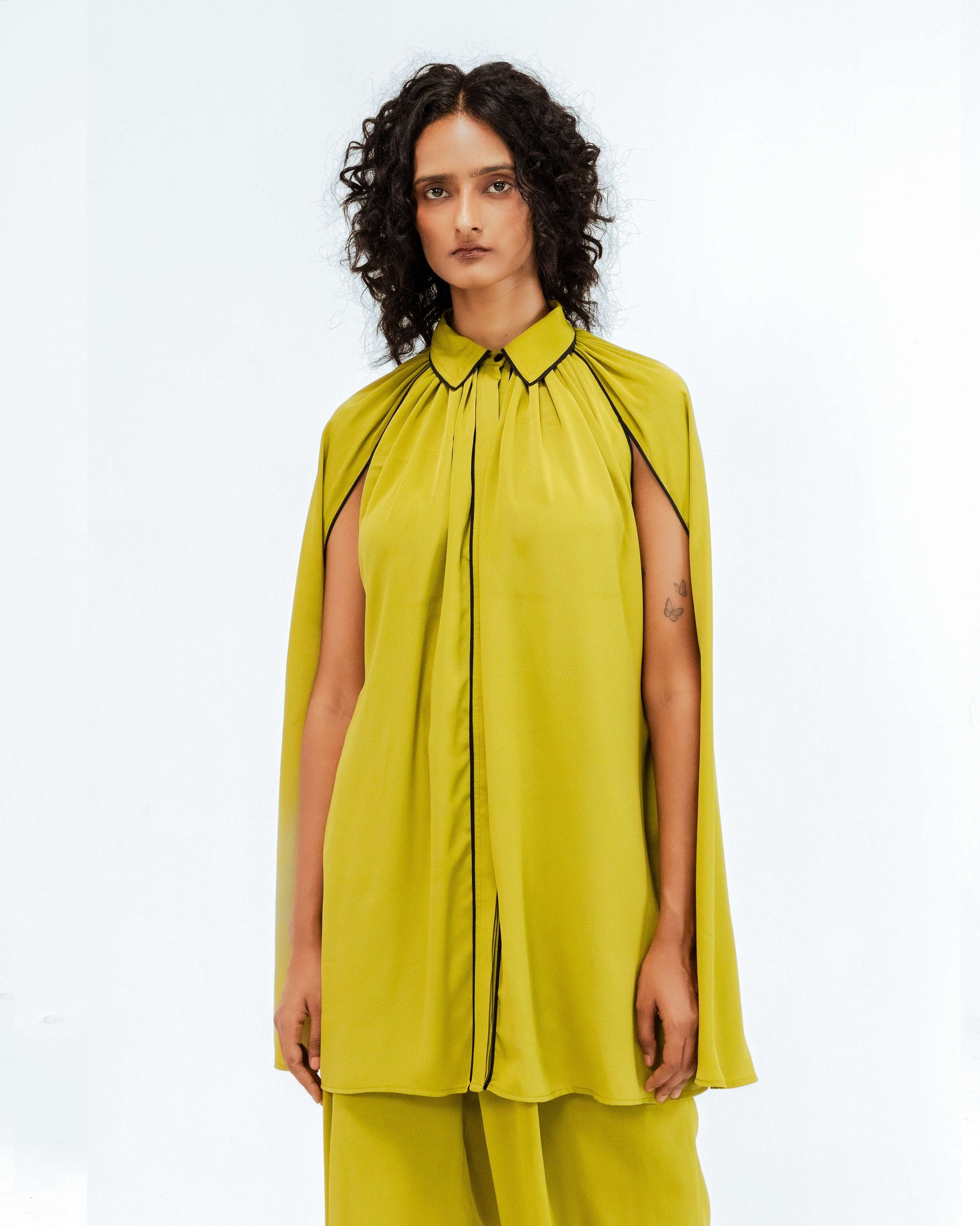 Leh Studios Cherice Crepe Cordset from the Rhythm of time collection. A model showcases this vibrant lime green sustainable fashion women's apparel with striking black piping details, featuring unique cape-like sleeves and elegantly tailored trousers. This piece exemplifies contemporary designer wear and eco-friendly design.