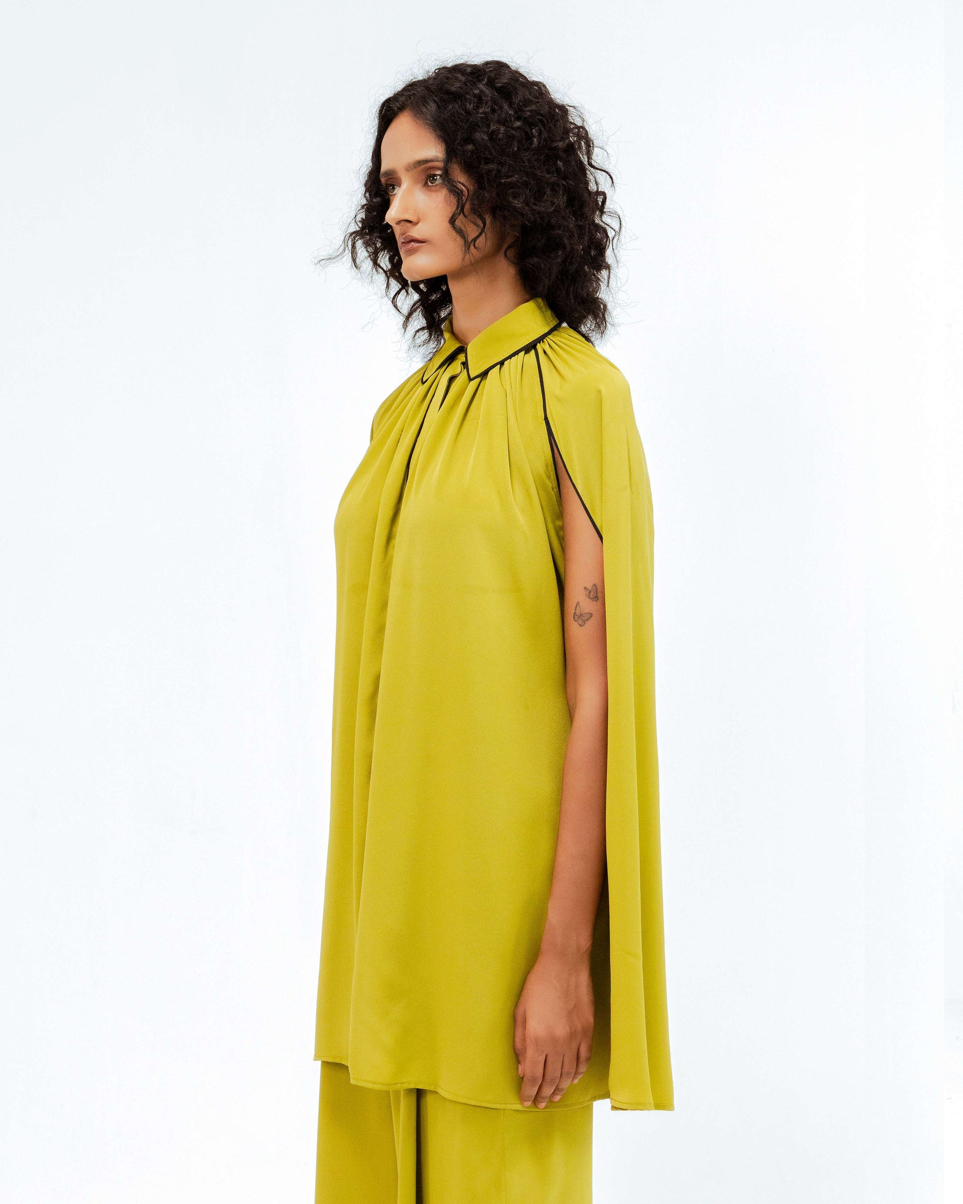 A model showcases the Cherice Crepe Cordset by Leh Studios, from the Rhythm of time collection. This chartreuse green ensemble features a sophisticated high-neck top with elegant cape-style sleeves and black piping detail, paired with fluid wide-leg pants. This designer wear piece highlights sustainable fashion and artisanal craftsmanship in contemporary womens apparel.