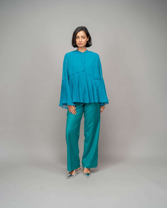 A person standing wearing blue pants and a matching blue top with a round neckline and long sleeves.